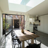 Dining table below skylight and open swivel door leading to courtyard