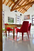 Modern red upholstered chairs around old wooden table below exposed roof structure