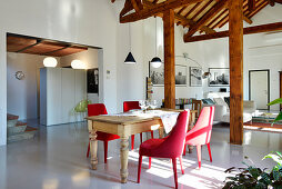 Red upholstered chairs around old wooden table in open-plan interior