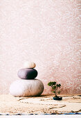 Felt pebbles and a bonsai on sand against pink wallpaper