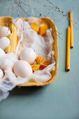 weiße Eier, Mulltuch und gelbe Papierrosetten in gelbem Eierkarton