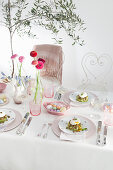 Festlicher Ostertisch mit Blumen in Glasvasen und Ostereier in einem Porzellankörbchen