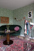 Round wooden table, velvet sofa and clothes rail against green wallpaper