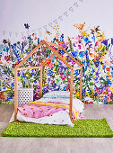 Bed frame in house shape in front of non-woven wallpaper with flower meadow in the children's room