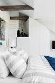 Double bed below rustic wooden beams in white bedroom