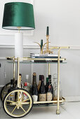 Table lamp and drinks on brass serving trolley against pale grey wall