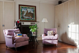 Two lilac armchairs in front of open fireplace and next to cupboard