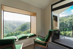 Grüne Polstersessel und passende Kissen auf Fensterbank vor Panoramafenster mit Landschaftsblick