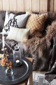 Fur blanket and cushions on sofa behind autumnal arrangement on coffee table