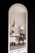 View through round arch on dining table, chair, bench and side table with table lamp