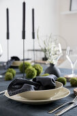 Table set with dark linens, beige crockery and handmade moss balls