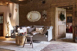 Grey sofa with scatter cushions, table with round glass top and wooden stools in rustic cabin