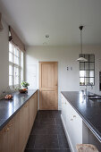 Unterschrank mit Holzfront vor Fenster und Mittelblock in Küche mit weißen Wänden und schwarzen Fliesenboden