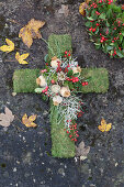 Mossy cross decorated with Gaultheria berries, poppy seedheads, silver ragweed and rose hips