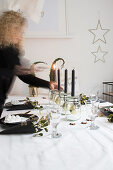 Frau zündet Kerzen an am weihnachtlich gedeckten Tisch