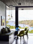 Sitzecke mit Bank, grünen Polsterstühlen und Tisch vor Glaswand mit Landschaftsblick