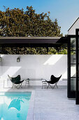 Klassikerstühle auf weißer, gemauerter Terrasse mit Pool