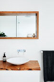 Designer-Waschschüssel auf Waschtisch mit Holzplatte, darüber Wandnische mit Holzrahmen und Spiegel