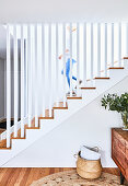 Treppe mit Geländer aus weißen Stelen, Sideboard mit Blätterzweig und Korbtasche auf dem Boden