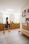 Barefoot woman walking through bright, open-plan kitchen with wooden cabinets