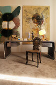 Schreibtisch mit Metallrahmen, antiker Holzstuhl mit Schnitzerei und moderne Kunst an der Wand