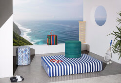 Mattress and pouf with colorful covers on terrace with sea view