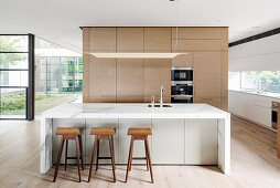 Designerküche mit Mittelblock aus Marmor und Barhockern in offenem Wohnraum mit Glasfront