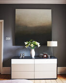 Painting with gradient of greys on grey wall above chest of drawers