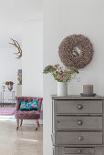 Grey chest of drawers with autumnal decorations and antique lilac armchair with blue scatter cushion in background