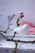 Weisser Dekovogel aufgehängt an Zweigen als winterliche Gartendekoration