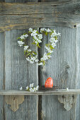 Kirschblütenkranz und handbemaltes rotes Osterei auf Regal vor rustikaler Holzwand