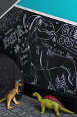 Toy dinosaurs in front of drawings on chalkboard in child's bedroom