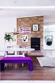 Violet upholstered bench at the dining table in front of the brick fireplace