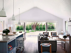 Kücheninsel mit Barhockern und Lounge mit Ledersofa und Rattanstühlen in offenem Wohnraum mit Terrassenzugang