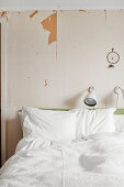 White bed linen on double bed below reading lamps and dreamcatcher on wall with peeling paint