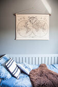 Bed with blue bed linen and sheepskin rug below vintage maps on wall