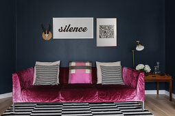 Pink, velvet couch with scatter cushions on black-and-white striped rug against dark wall