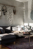 Couchtisch, Sofa, darüber Traumfänger, Sessel und Paravent im Wohnzimmer mit hellgrauer Wand