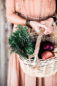 Woman in nostalgic dress carries basket with sprigs of rosemary and harvest