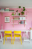 Yellow chairs at desk below shelves on pink wall