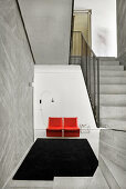 Red armchair, arc lamp and side table in foyer with concrete stairs in foreground