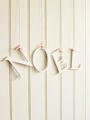 Die Buchstaben 'Noel' als Schriftzug aufgehängt vor weisser Holzwand