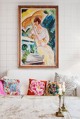 Colourful scatter cushions on sofa below painting on tiled wall