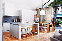 Open kitchen with kitchen island and dining area in front of patio door, family with small child at the dining table