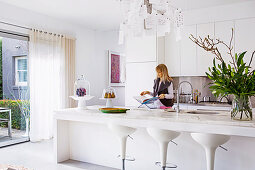 White fitted kitchen with island and bar stools, woman in the background