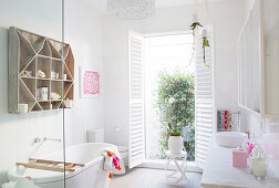 Shelf over bathtub, toilet, open shutters and vanity in bright bathroom