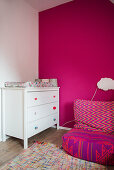 Changing mat on white chest of drawers and beanbag in room with hot-pink wall