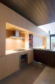Modern fitted kitchen in pale wood with dark wooden ceiling