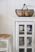 Wire basket on top of small cupboard with wire door panels holding crockery