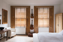Classical guitars hung up on wall of bedroom with pine window shutters and white armchair